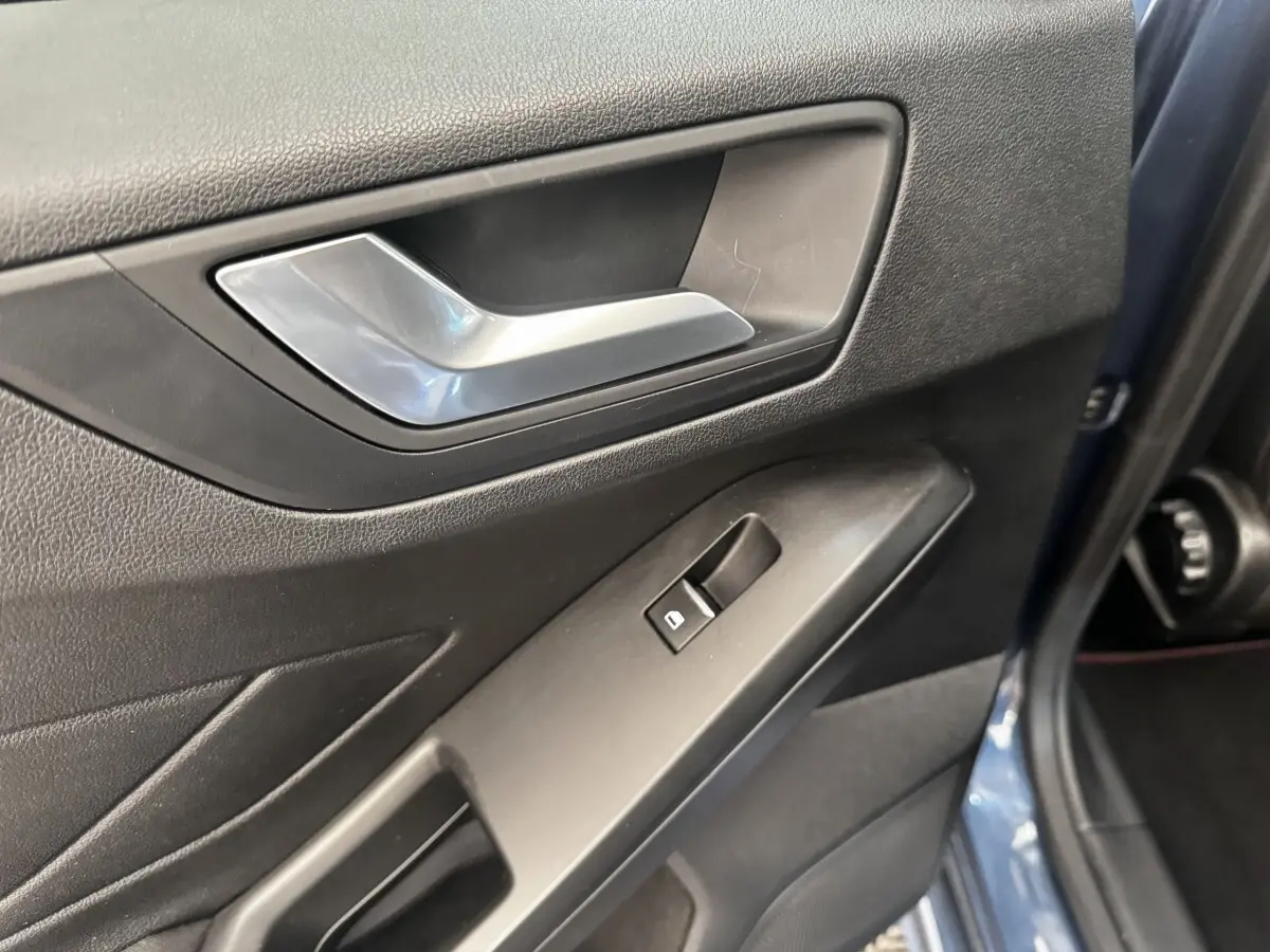 Gros plan sur la poignée intérieure et le bouton de lève-vitre côté conducteur d'une Ford Focus bleu 5 portes.