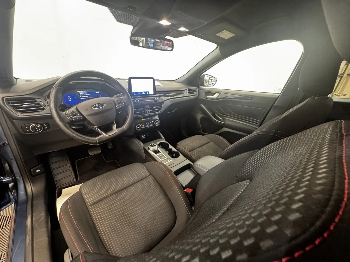 Vue intérieure côté conducteur de la Ford Focus St-Line 2022, sièges noirs avec surpiqûres rouges et écran tactile central.