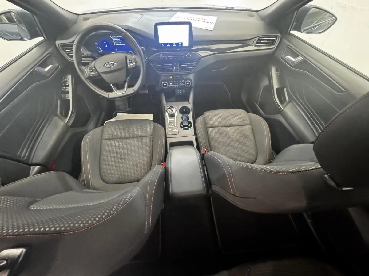 Vue intérieure avant de la Ford Focus 5P St-Line 2022, sièges noirs avec surpiqûres rouges et tableau de bord numérique.
