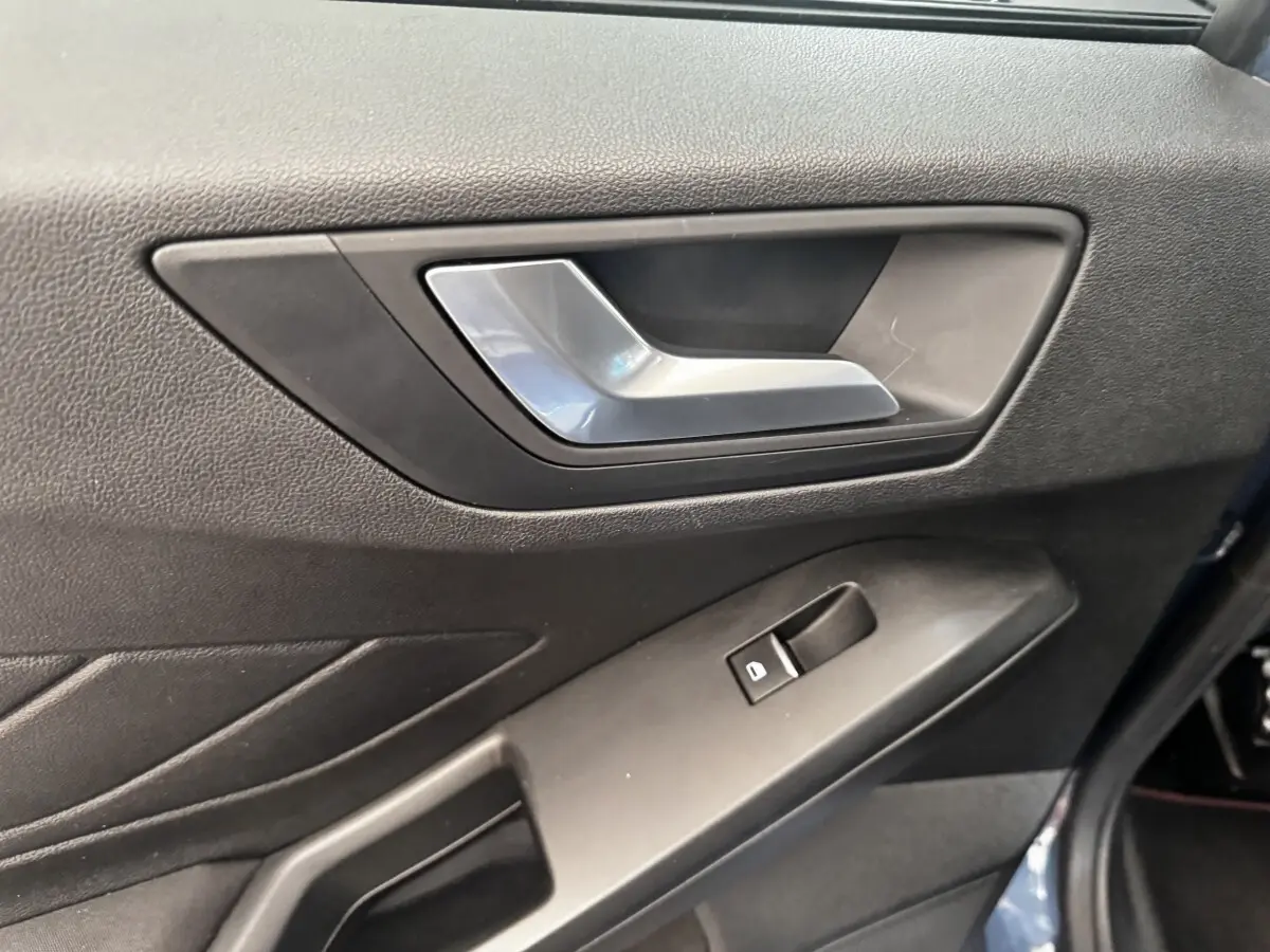 Gros plan sur la poignée intérieure et la commande de vitre côté gauche d'une Ford Focus bleu 5 portes 2022.