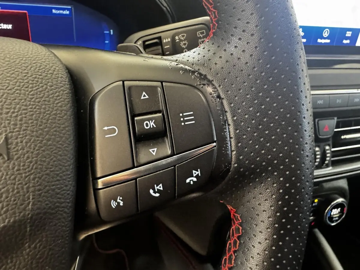 Gros plan sur les commandes gauche du volant en cuir noir perforé avec surpiqûres rouges de la Ford Focus bleu 2022.