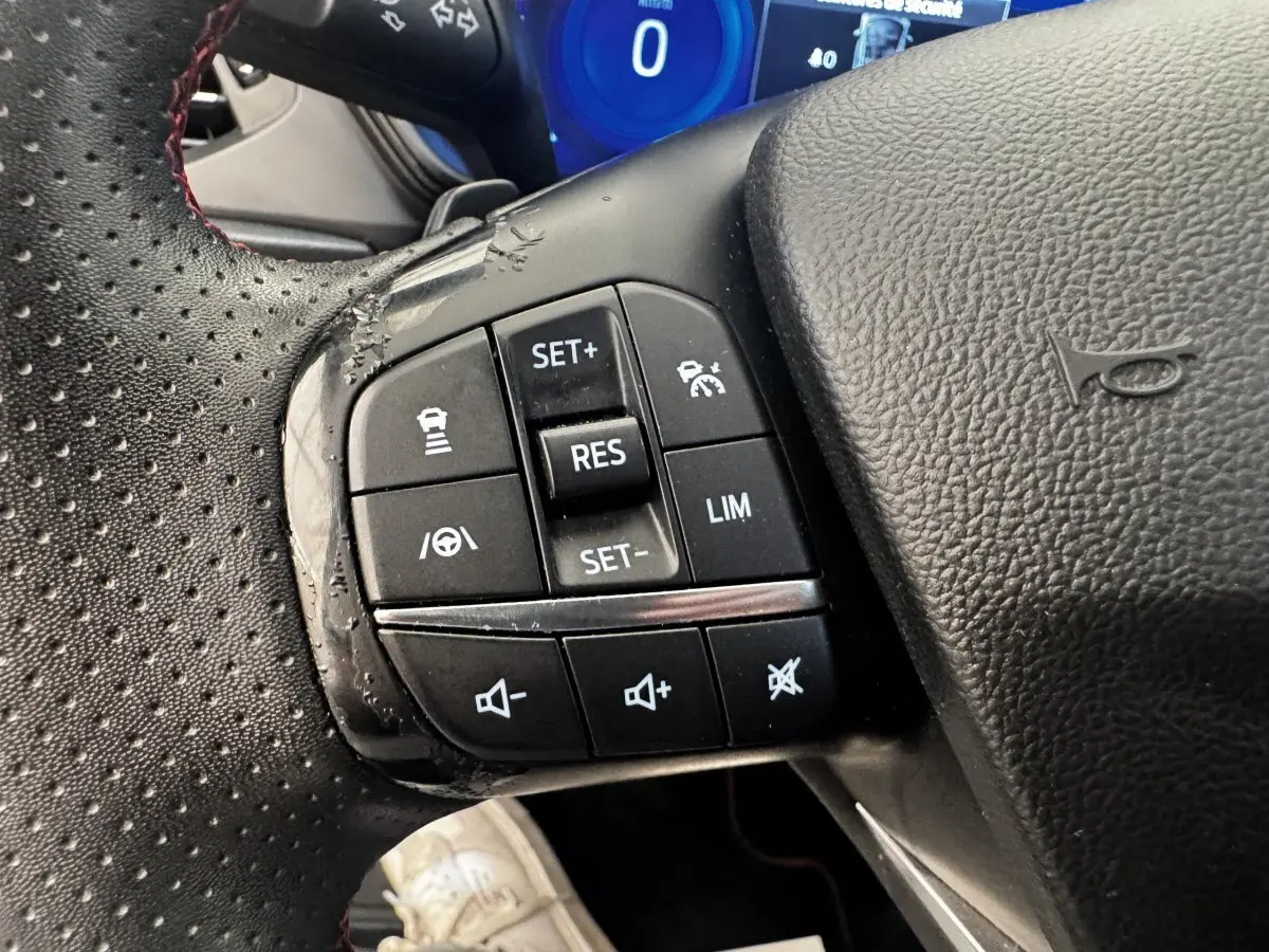 Gros plan sur les commandes multifonctions à gauche du volant cuir perforé d'une Ford Focus bleu 2022.