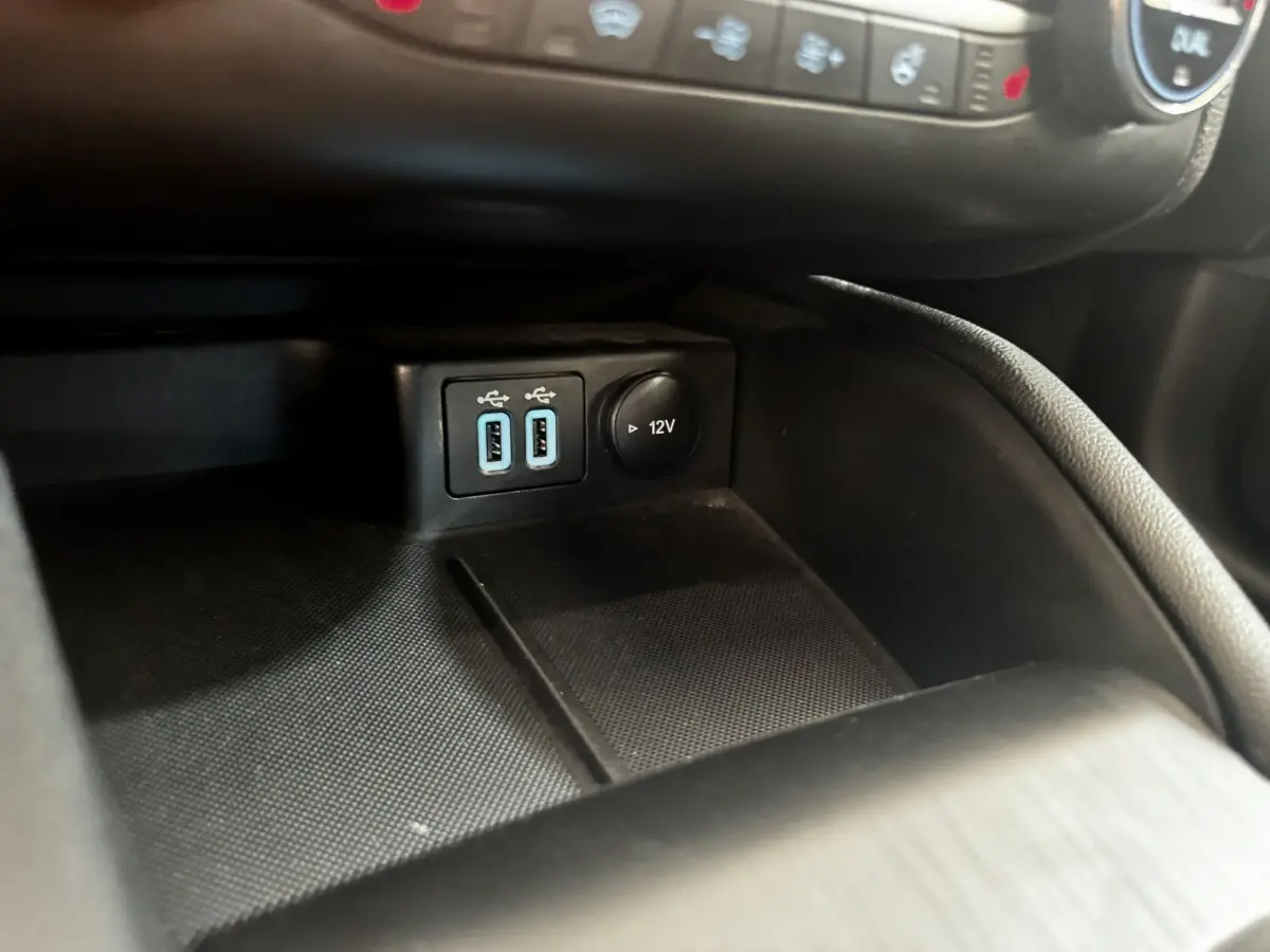 Gros plan sur la console centrale noire de la Ford Focus 5P avec prises USB doubles et prise 12V visible.