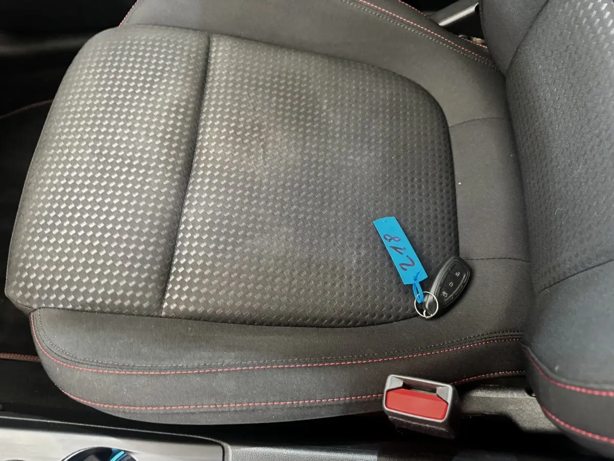 Gros plan sur le siège avant droit en tissu noir avec surpiqûres rouges et clé de voiture Ford posée dessus.
