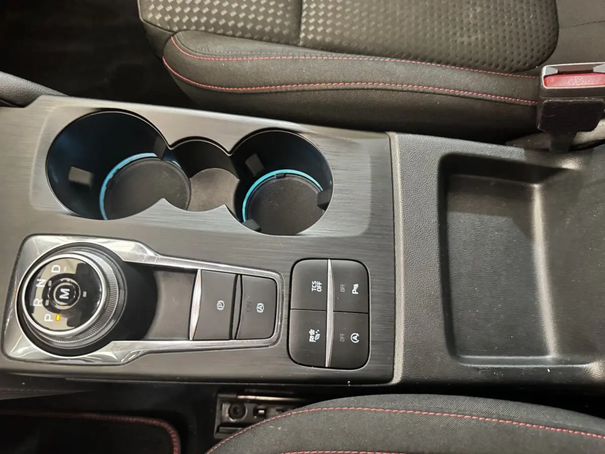 Vue plongeante sur la console centrale noire de la Ford Focus St-Line 2022 avec molette de boîte auto et porte-gobelets.