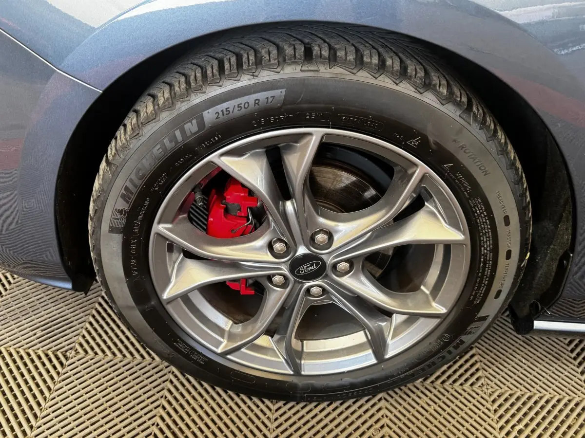 Gros plan sur la roue avant droite d’une Ford Focus bleu, jante alliage grise avec étrier de frein rouge visible.