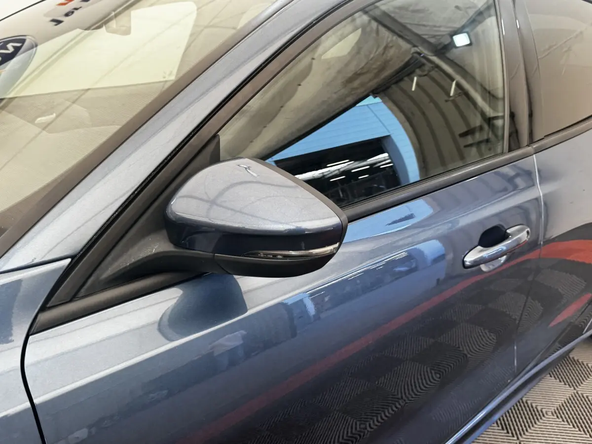 Gros plan sur le rétroviseur côté gauche et la porte avant bleu métallisé d’une Ford Focus 5P St-Line 2022.
