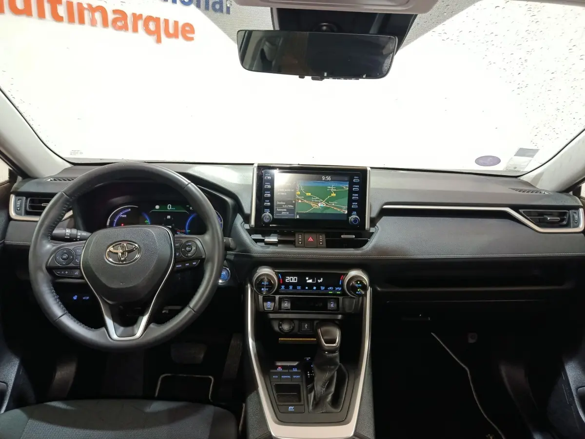 Vue intérieure frontale du tableau de bord noir du Toyota RAV4 hybride avec écran tactile central et volant cuir multifonctions.