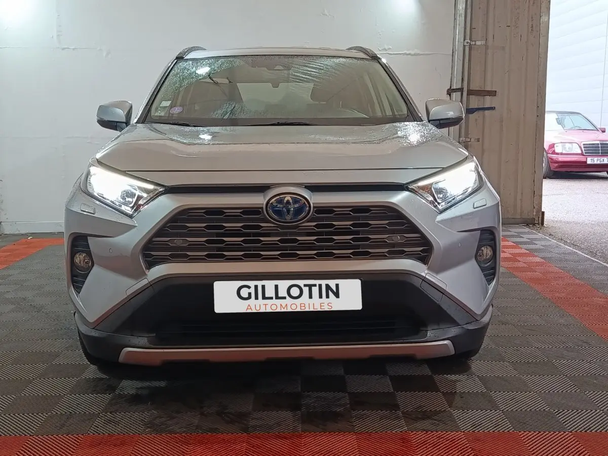 Vue frontale du Toyota RAV4 hybride gris clair avec calandre hexagonale et feux LED allumés dans un garage.