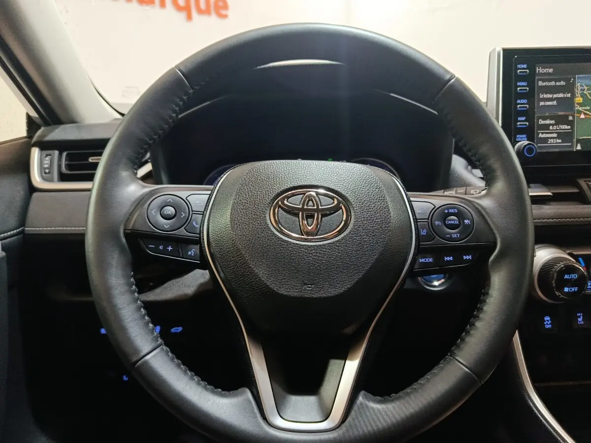 Vue rapprochée du volant cuir noir du Toyota RAV4 hybride 2021 avec commandes multifonctions et tableau de bord digital.