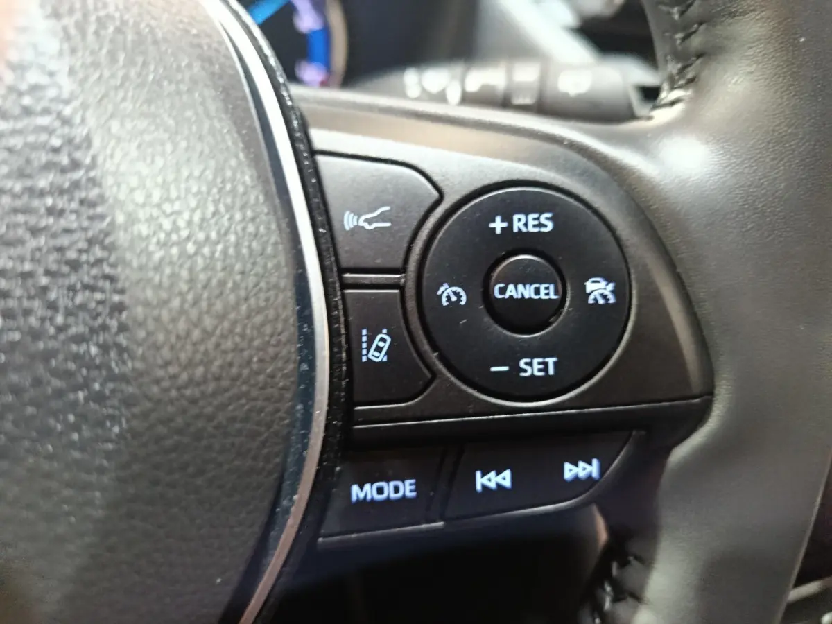 Gros plan sur les commandes au volant côté droit du Toyota RAV4 hybride, avec boutons de régulateur et mode audio.