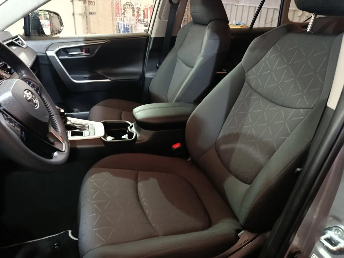 Vue intérieure côté conducteur du Toyota RAV4 Hybride 2WD 218ch Dynamic 2021 avec sièges tissu gris et console centrale noire.
