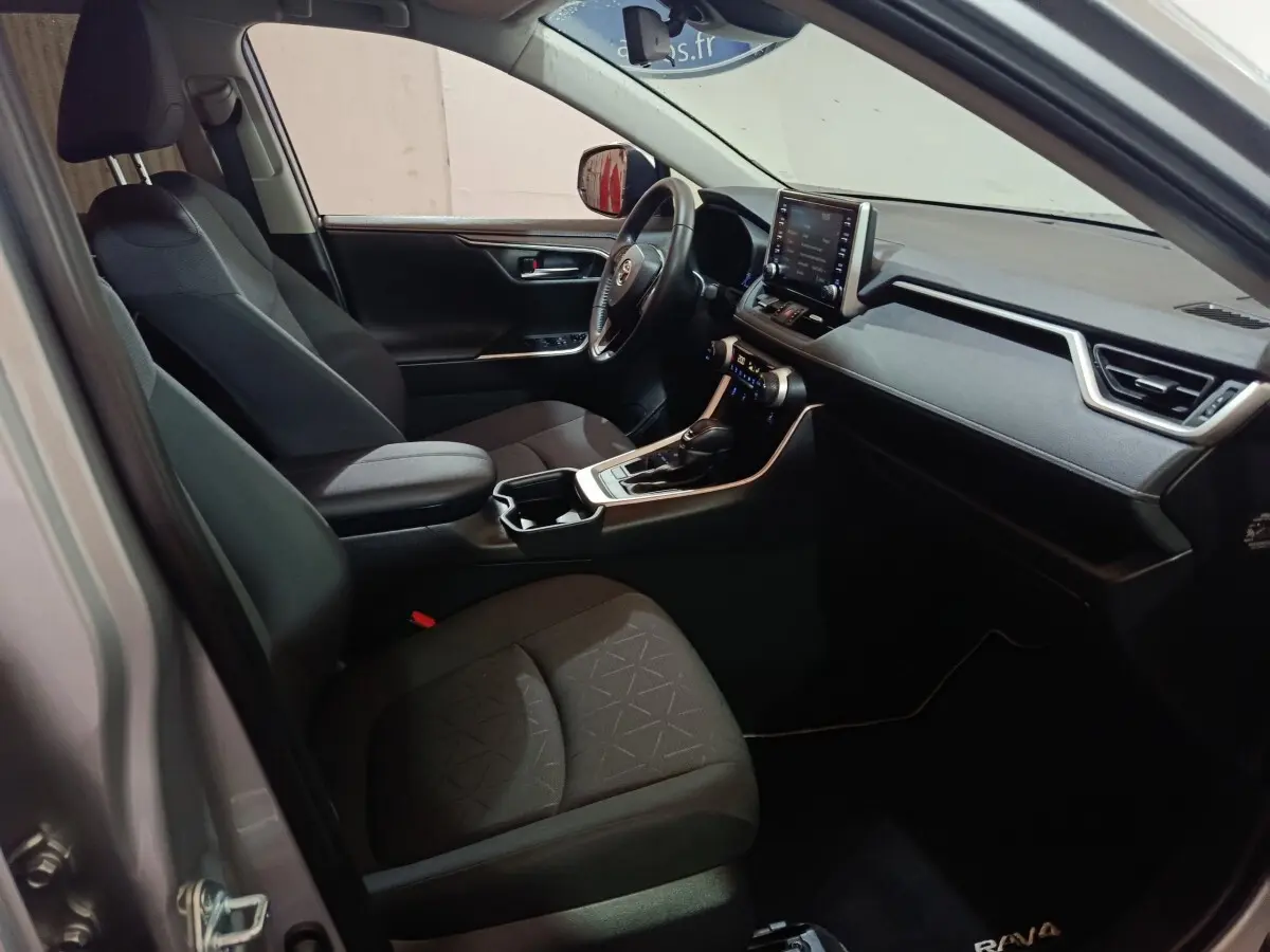 Vue intérieure côté conducteur du Toyota RAV4 hybride 2021, sièges noirs et tableau de bord avec écran tactile central.