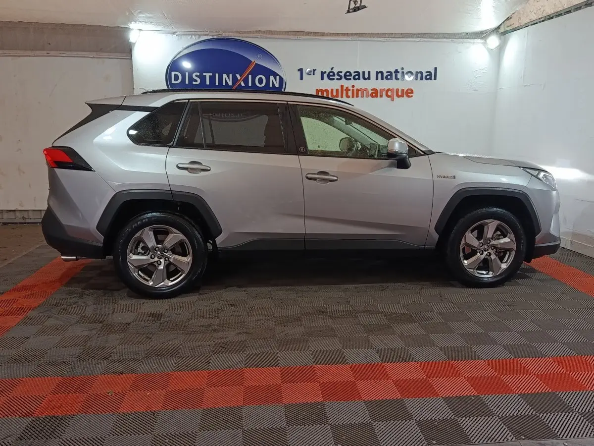 Profil droit du Toyota RAV4 hybride 2WD 2021 gris clair avec jantes alliage et protections noires sur les passages de roues.