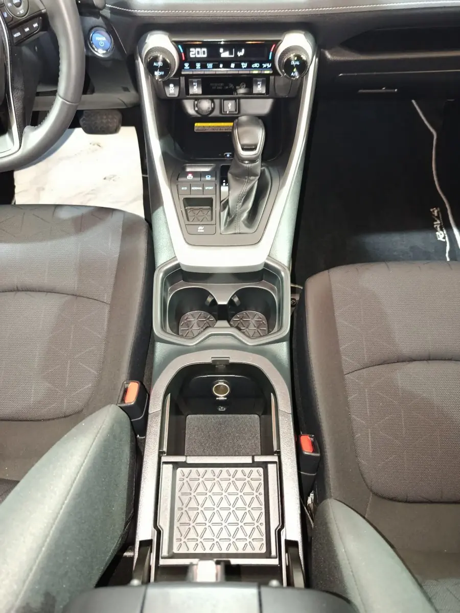 Vue plongeante sur la console centrale noire du Toyota RAV4 hybride avec levier de vitesse et sièges tissu gris.
