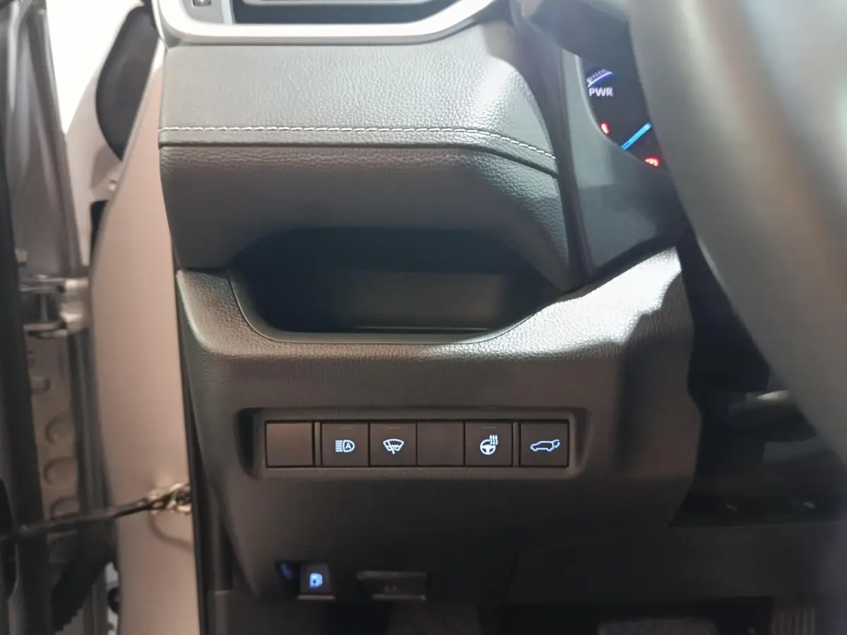 Vue rapprochée du tableau de bord côté gauche du Toyota RAV4 hybride 2021, boutons de commandes éclairés sur plastique noir.