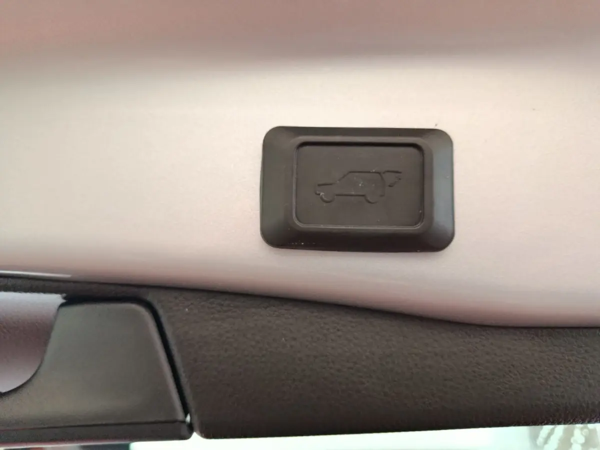 Gros plan sur le bouton d'ouverture électrique du coffre du Toyota RAV4 Hybride 2WD 218ch Dynamic, intérieur noir et beige.