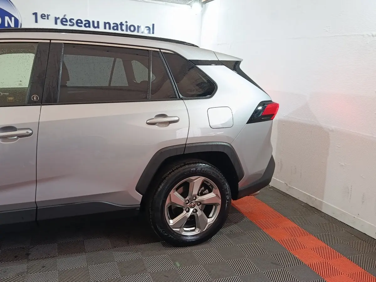 Vue latérale droite arrière d'un Toyota RAV4 hybride gris clair avec jantes alliage et feux arrière LED.