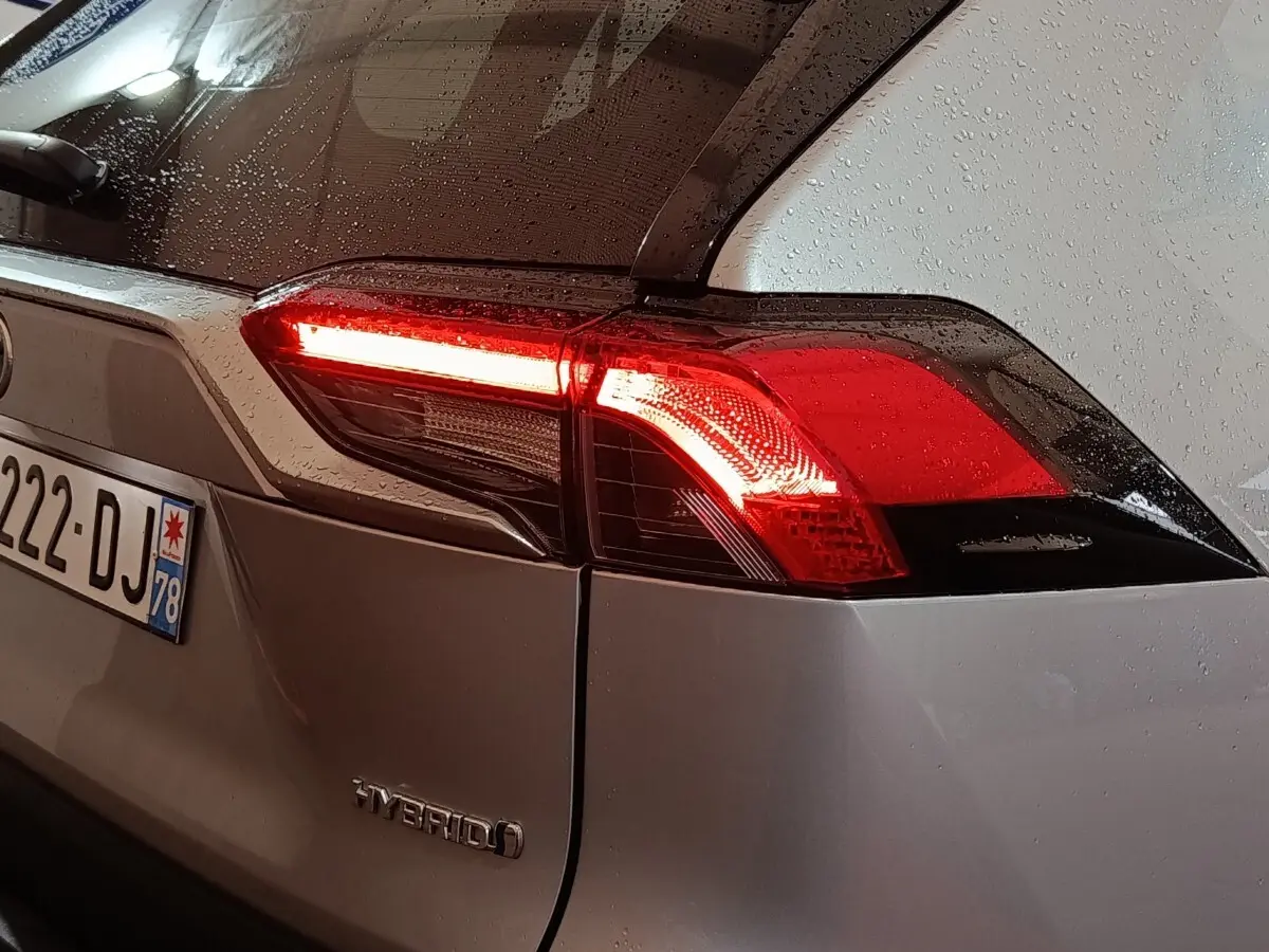 Vue arrière droite du Toyota RAV4 hybride gris avec feu arrière allumé et pluie sur la carrosserie.
