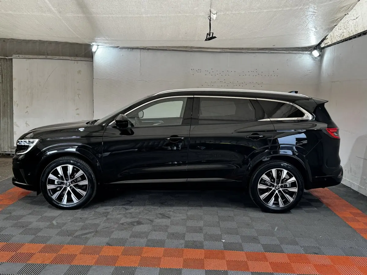 Profil côté gauche d’un Renault Espace noir 2025 avec rails de toit chromés dans un garage.