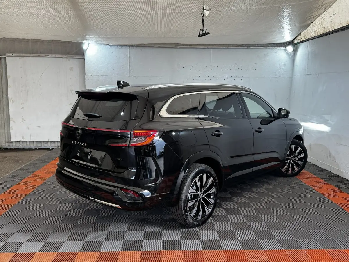 Renault Espace noir en 3/4 arrière droit, avec rails de toit chromés et feux arrière LED allumés dans un garage.