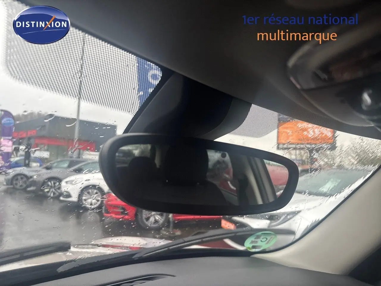 Vue intérieure du rétroviseur central d'une MINI 1.5 136CH grise, avec pluie visible sur le pare-brise.