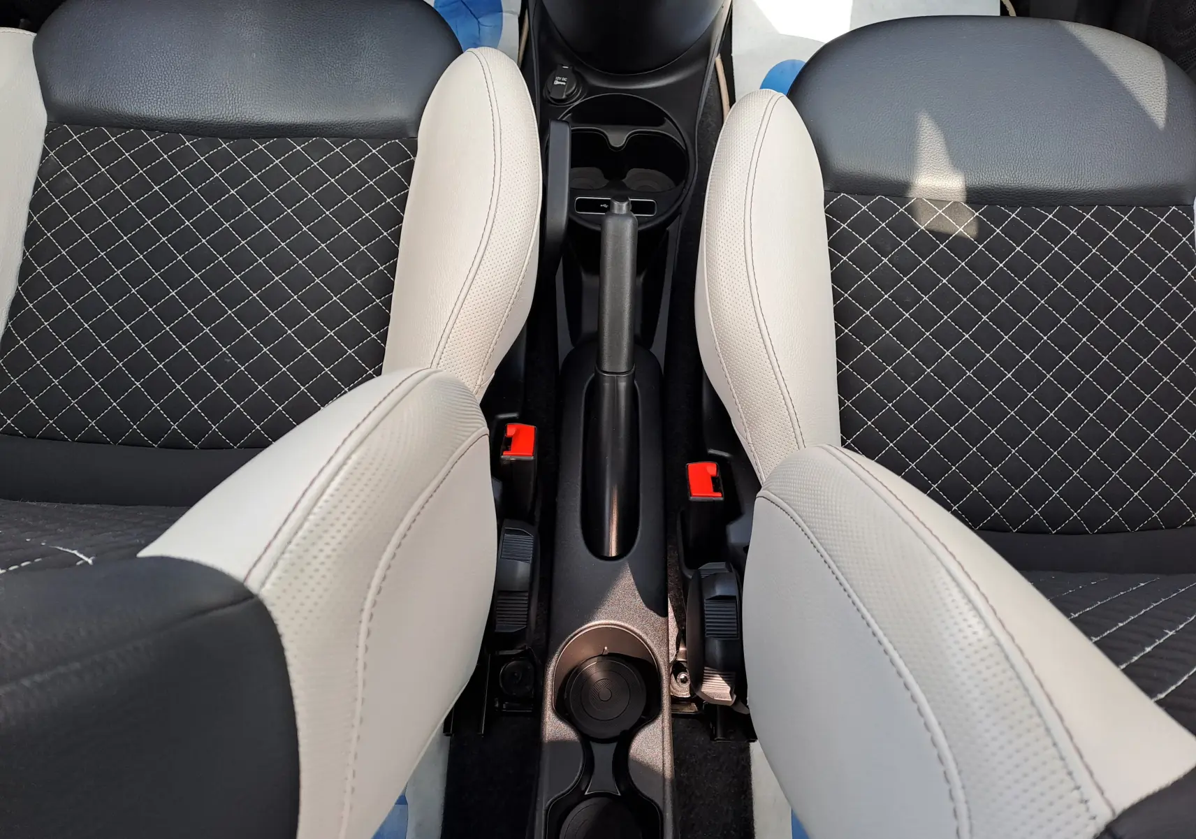 Vue plongeante sur les sièges avant noir et beige avec coutures croisées et console centrale d'une Fiat 500 2020.