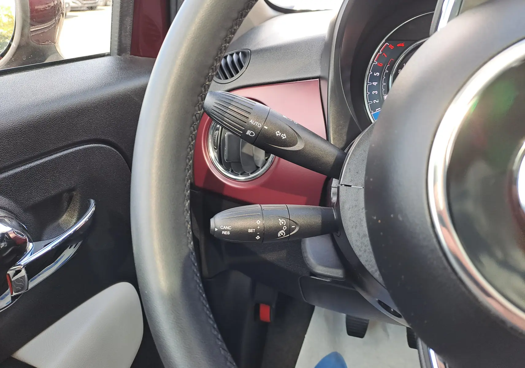 Vue rapprochée du volant et des commandes de la FIAT 500 2020, avec tableau de bord bordeaux Opera et intérieur noir.