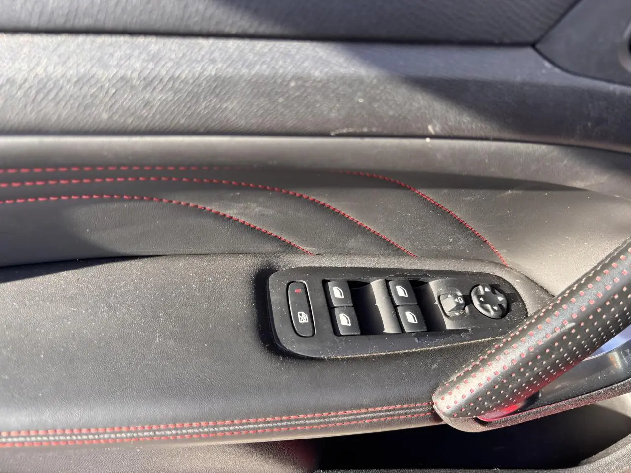 Détail des commandes de lève-vitres sur la porte côté gauche en cuir noir avec surpiqûres rouges de la Peugeot 308 GT Line.