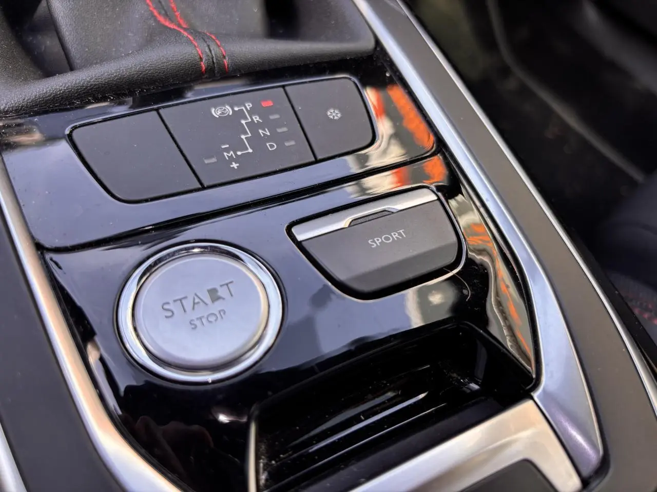 Gros plan sur la console centrale noire brillante de la Peugeot 308 GT Line avec bouton Start/Stop et touche Sport.