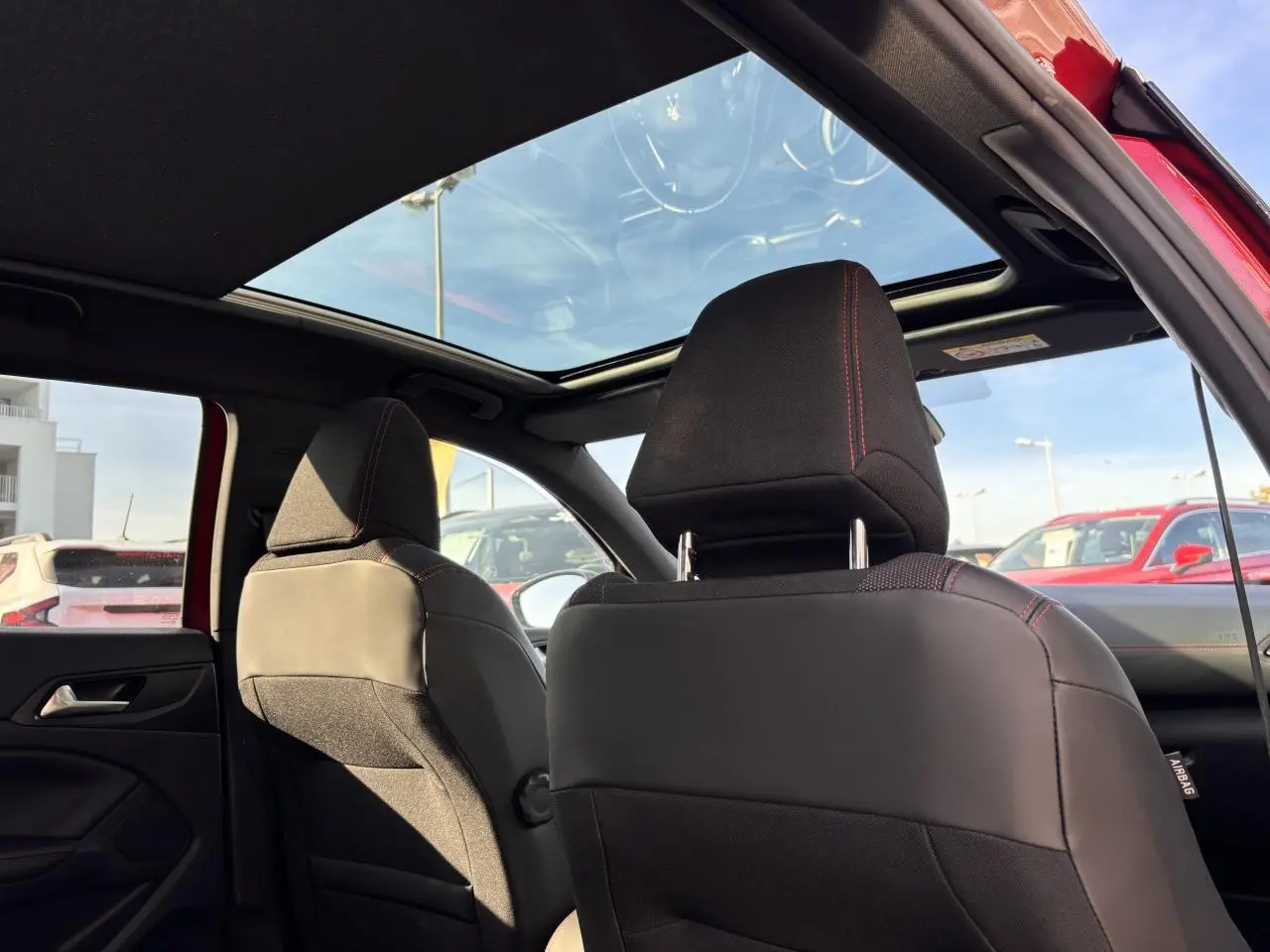 Vue intérieure arrière des sièges avant noirs avec surpiqûres rouges et toit panoramique en verre d'une Peugeot 308 rouge foncé GT Line.