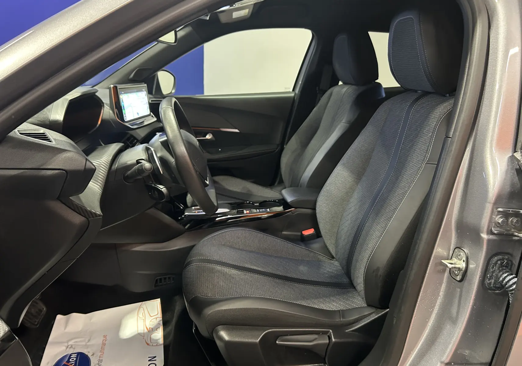 Vue intérieure côté conducteur du Peugeot 2008 gris 2025 avec sièges tissu et tableau de bord moderne équipé d'un écran tactile.