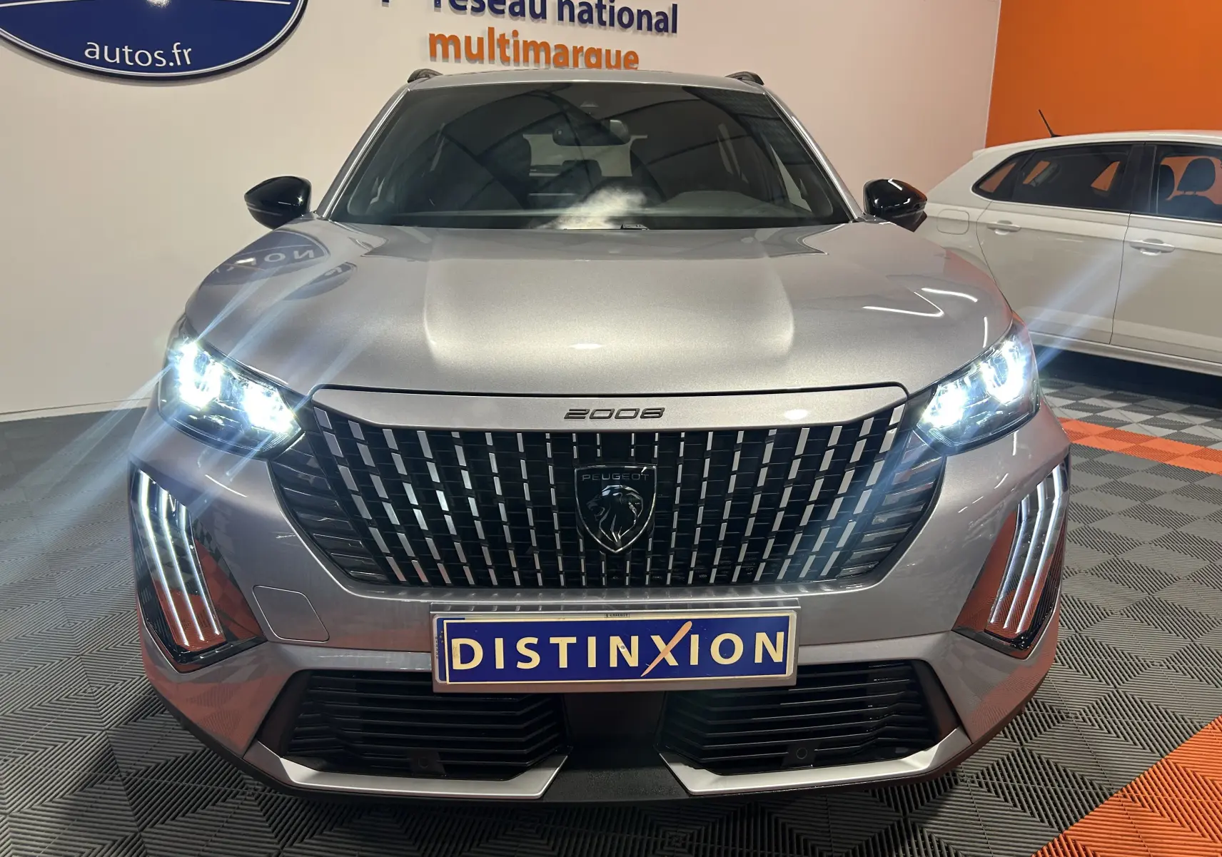 Vue frontale d'un Peugeot 2008 gris 2025 avec phares allumés et calandre noire distinctive en concession.