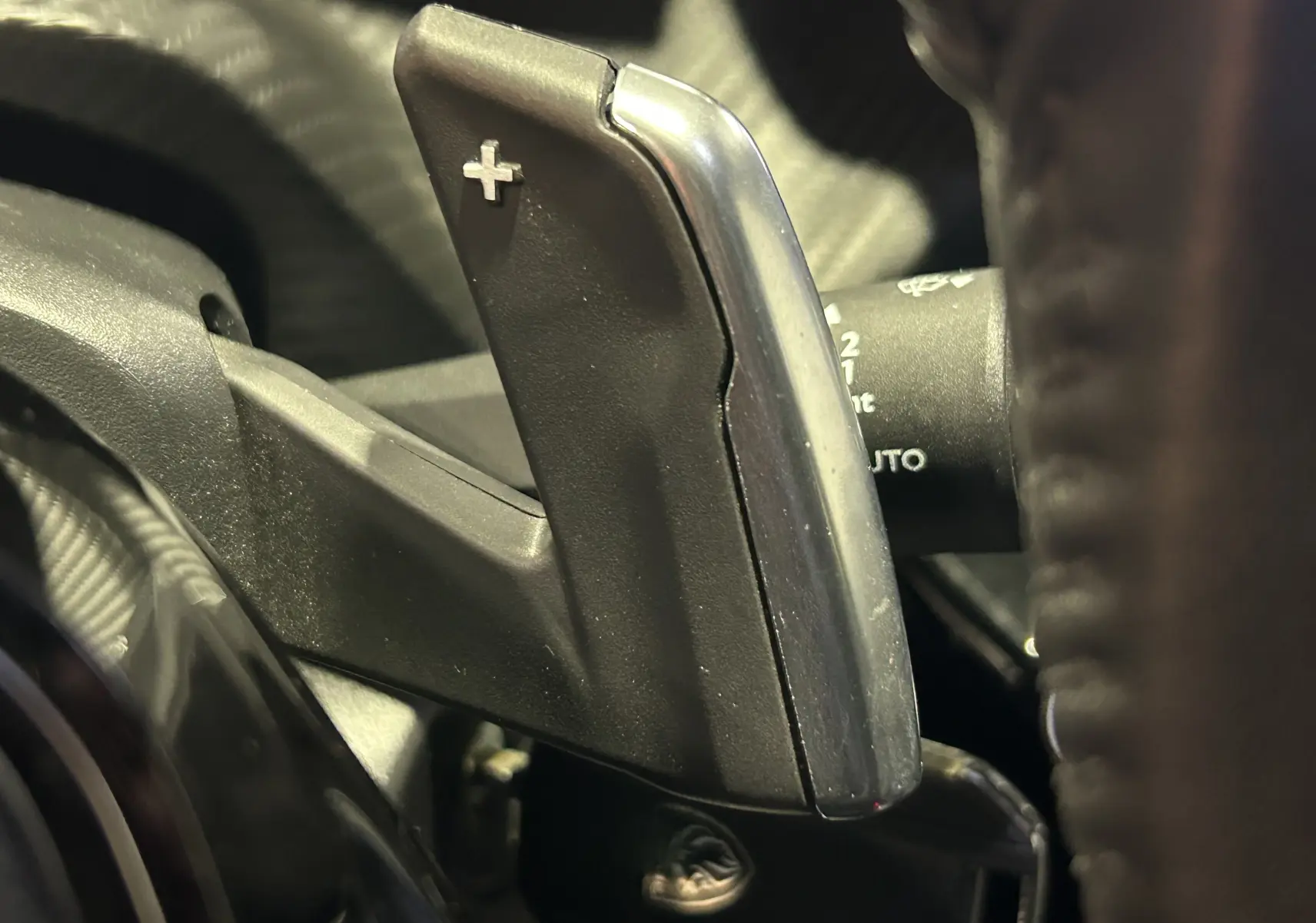 Gros plan sur la palette de changement de vitesse "+" côté droit du volant du Peugeot 2008 Allure Hybrid gris 2025.