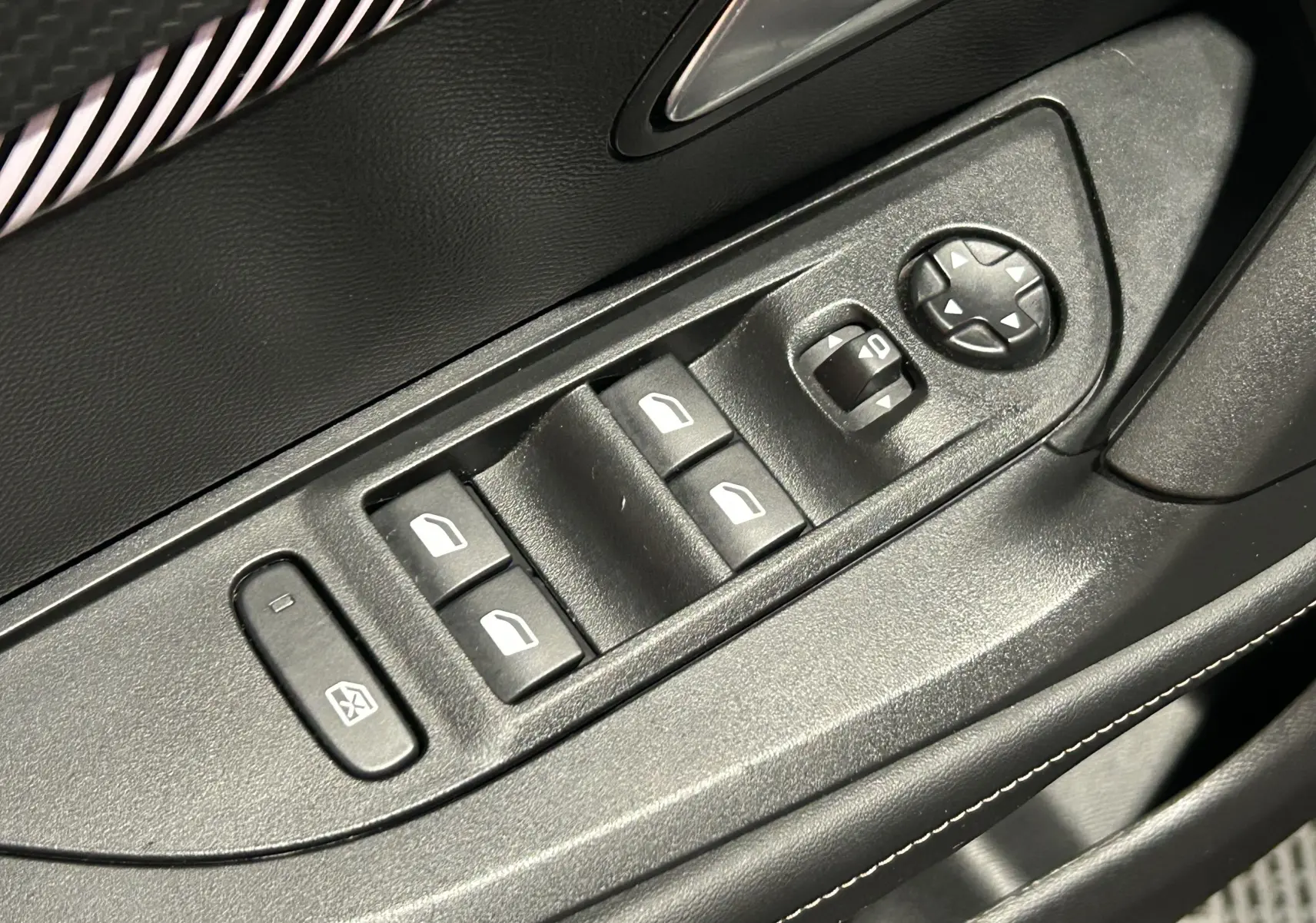 Gros plan sur les commandes de lève-vitres et réglage des rétroviseurs côté conducteur du Peugeot 2008 gris 2025.