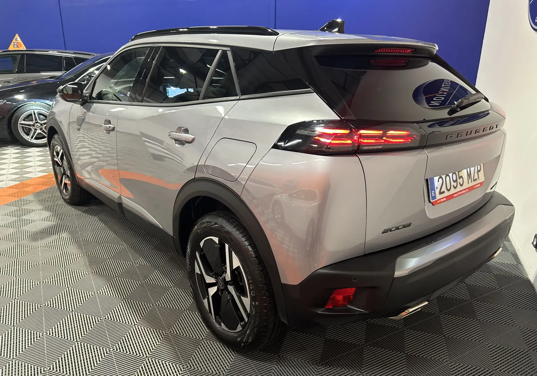Vue 3/4 arrière droite d'un Peugeot 2008 gris 2025 avec feux arrière LED allumés et jantes alliage noires.