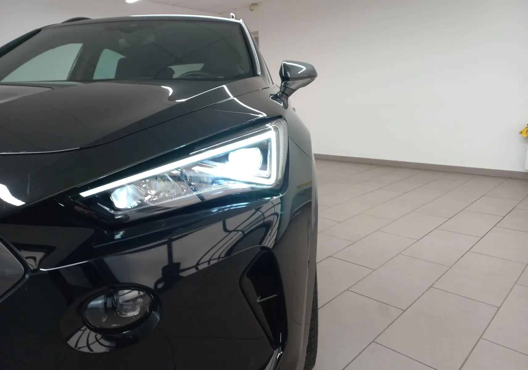 Gros plan sur le phare avant droit allumé d'une CUPRA Formentor 2023 noir minuit avec peinture métallisée brillante.