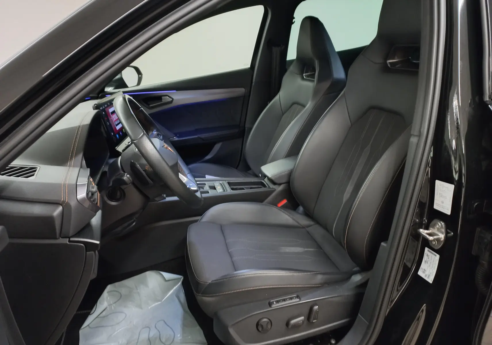 Vue intérieure côté conducteur de la CUPRA Formentor noir minuit, sièges sport en cuir avec éclairage d'ambiance bleu.