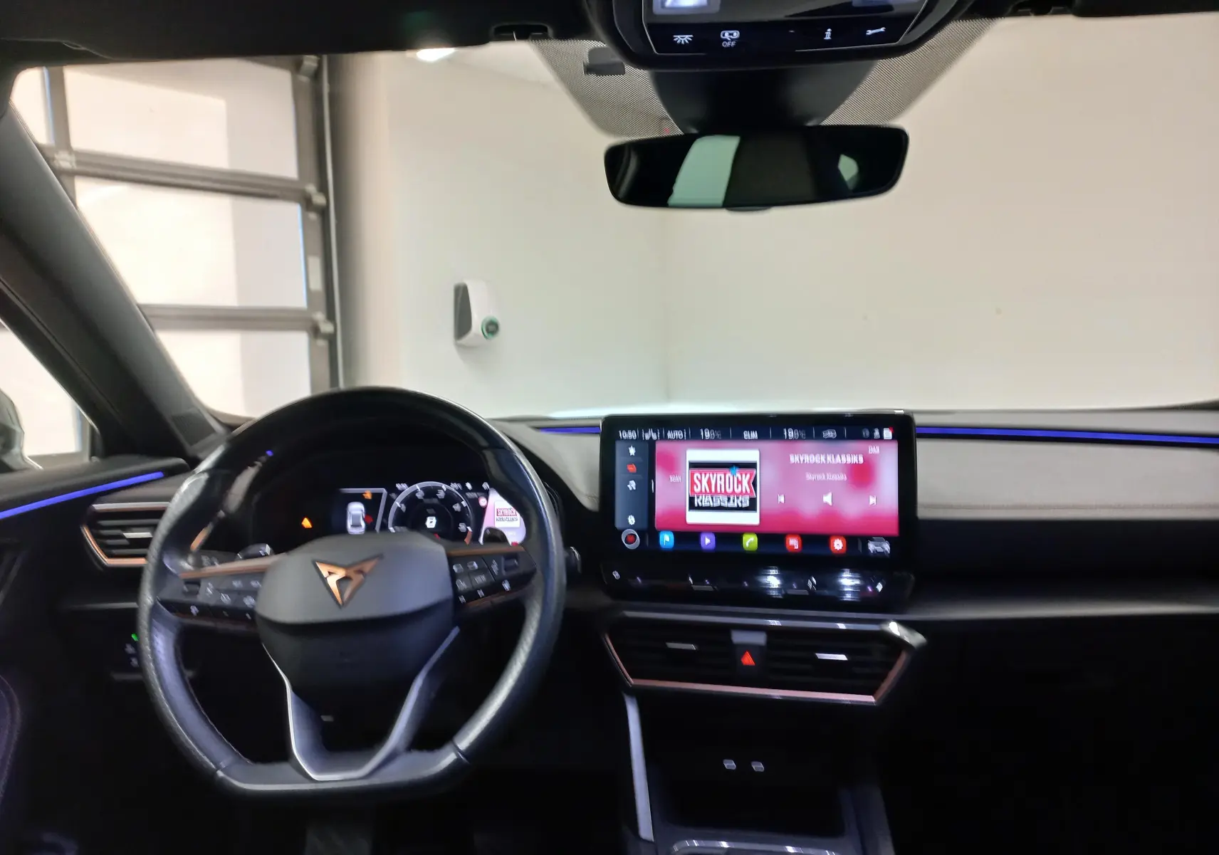 Vue intérieure du tableau de bord du CUPRA Formentor 2023, avec éclairage d'ambiance bleu et écran tactile central allumé.