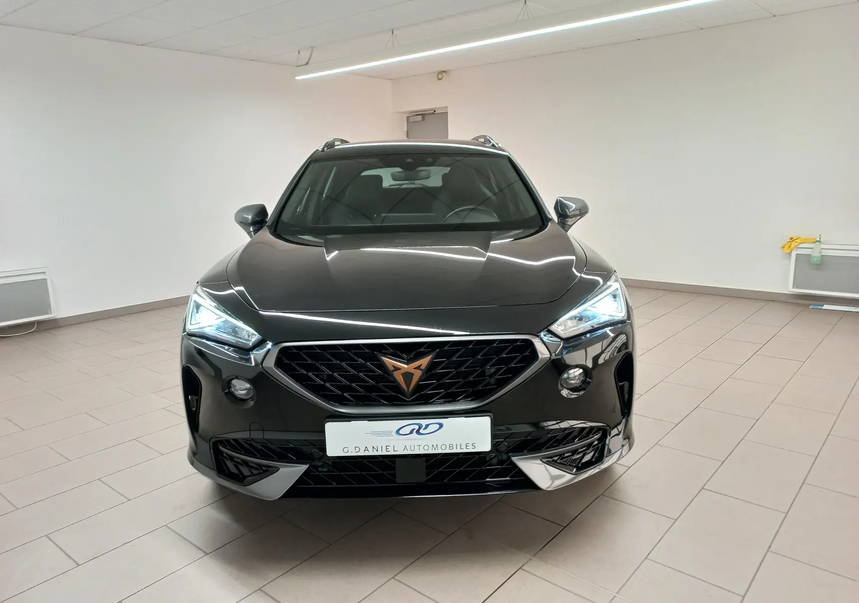 Vue avant frontale du CUPRA Formentor noir minuit avec calandre noire et logo cuivré, éclairage LED allumé en intérieur neutre.