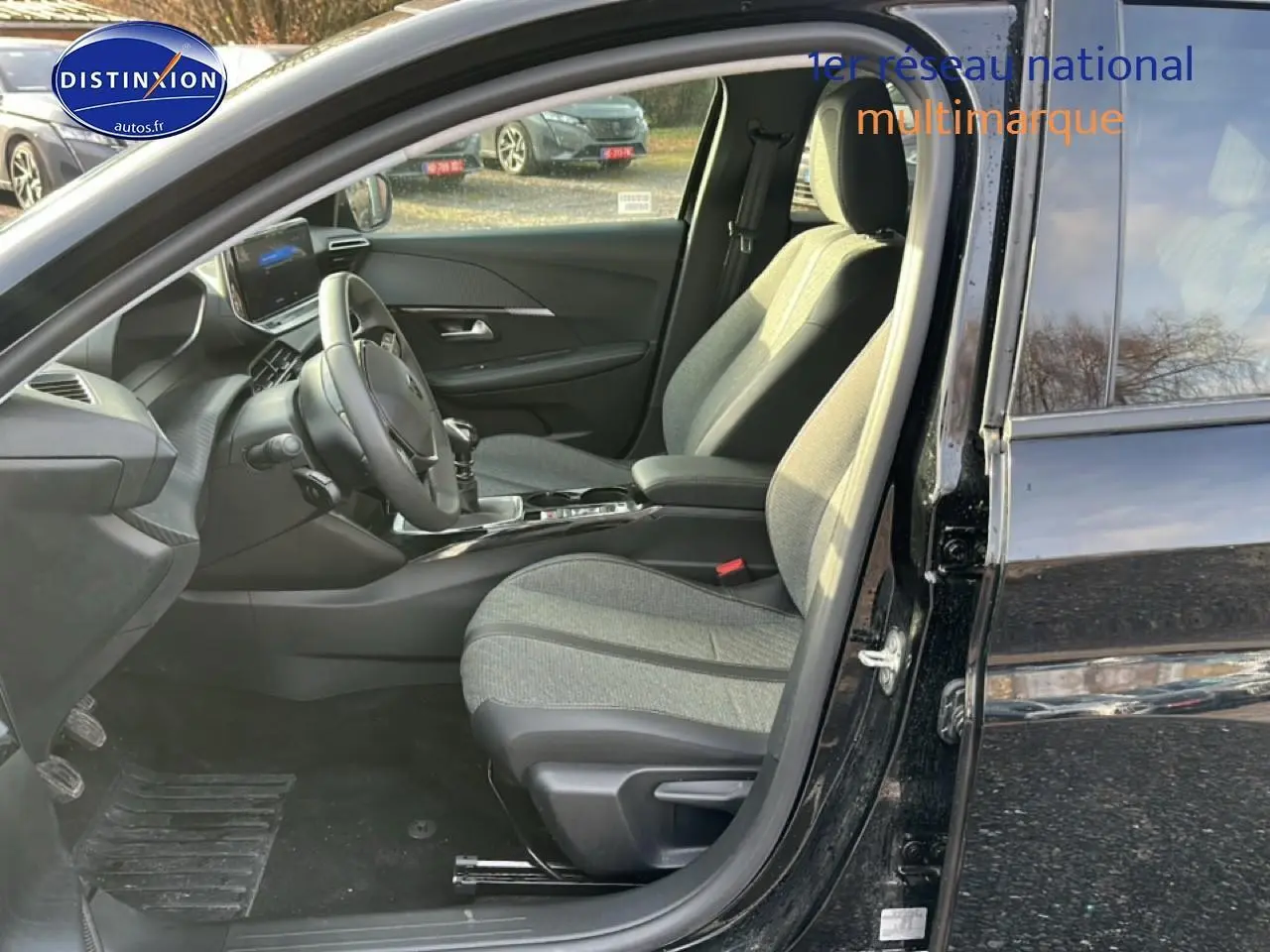 Intérieur de la Peugeot 208 1.2 PureTech 100 Allure 2024 noir, vue côté conducteur avec sièges tissu gris et volant multifonction.