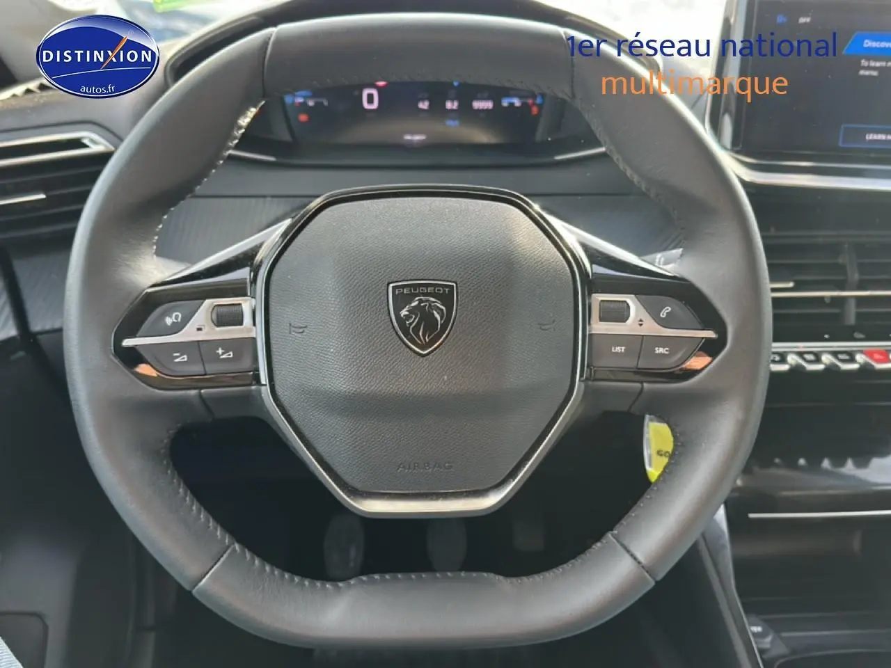 Vue rapprochée du volant noir de la Peugeot 208 1.2 PureTech 100 Allure 2024 avec commandes intégrées et tableau de bord numérique.