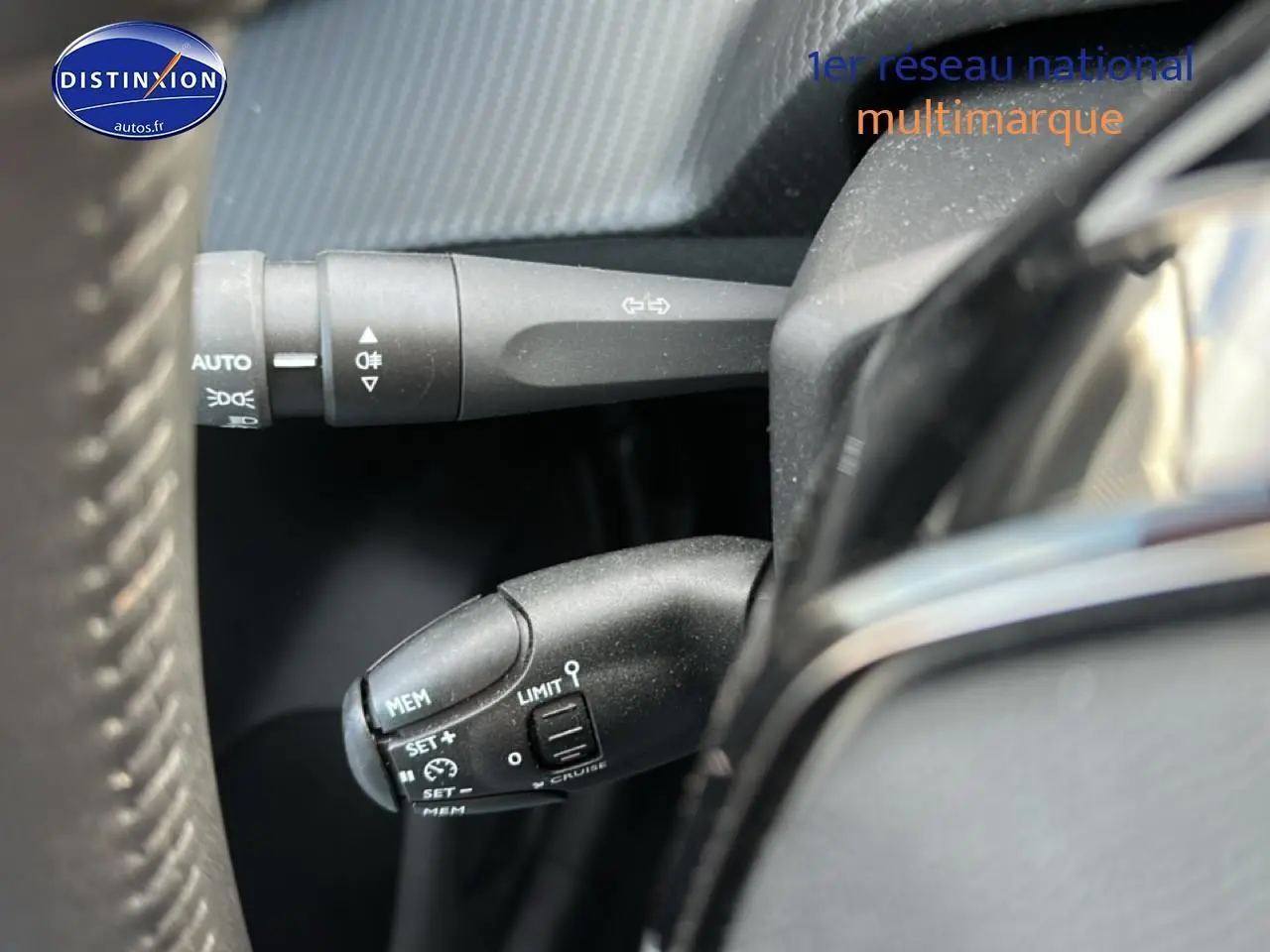 Gros plan sur les commandes au volant côté gauche d’une Peugeot 208 noire 2024, avec régulateur de vitesse et clignotants.