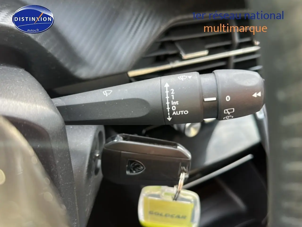 Gros plan sur la commande d'essuie-glace et la clé insérée dans le contact d'une Peugeot 208 noire, intérieur visible.