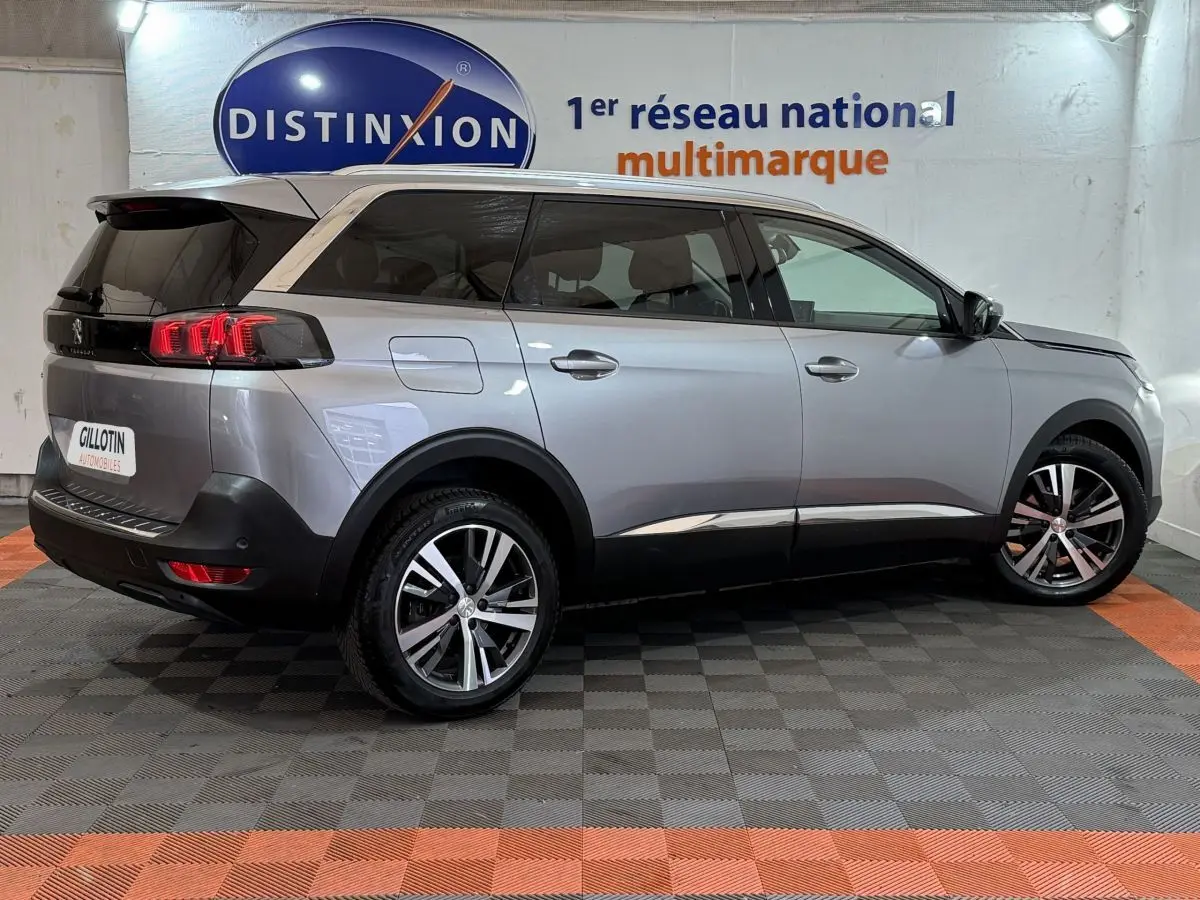 Peugeot 5008 gris clair en vue 3/4 arrière droit, avec feux arrière LED et jantes alliage bicolores.