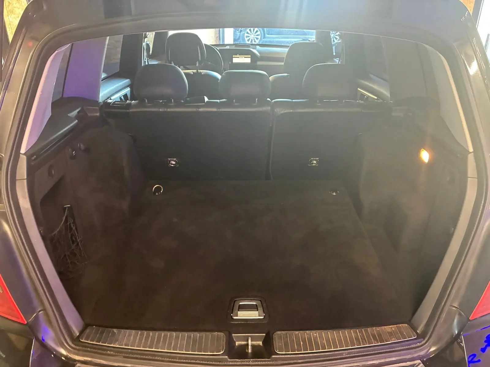 Coffre ouvert vu de l'arrière d'un Mercedes GLK noir, montrant l'espace de chargement et les sièges arrière en cuir noir.