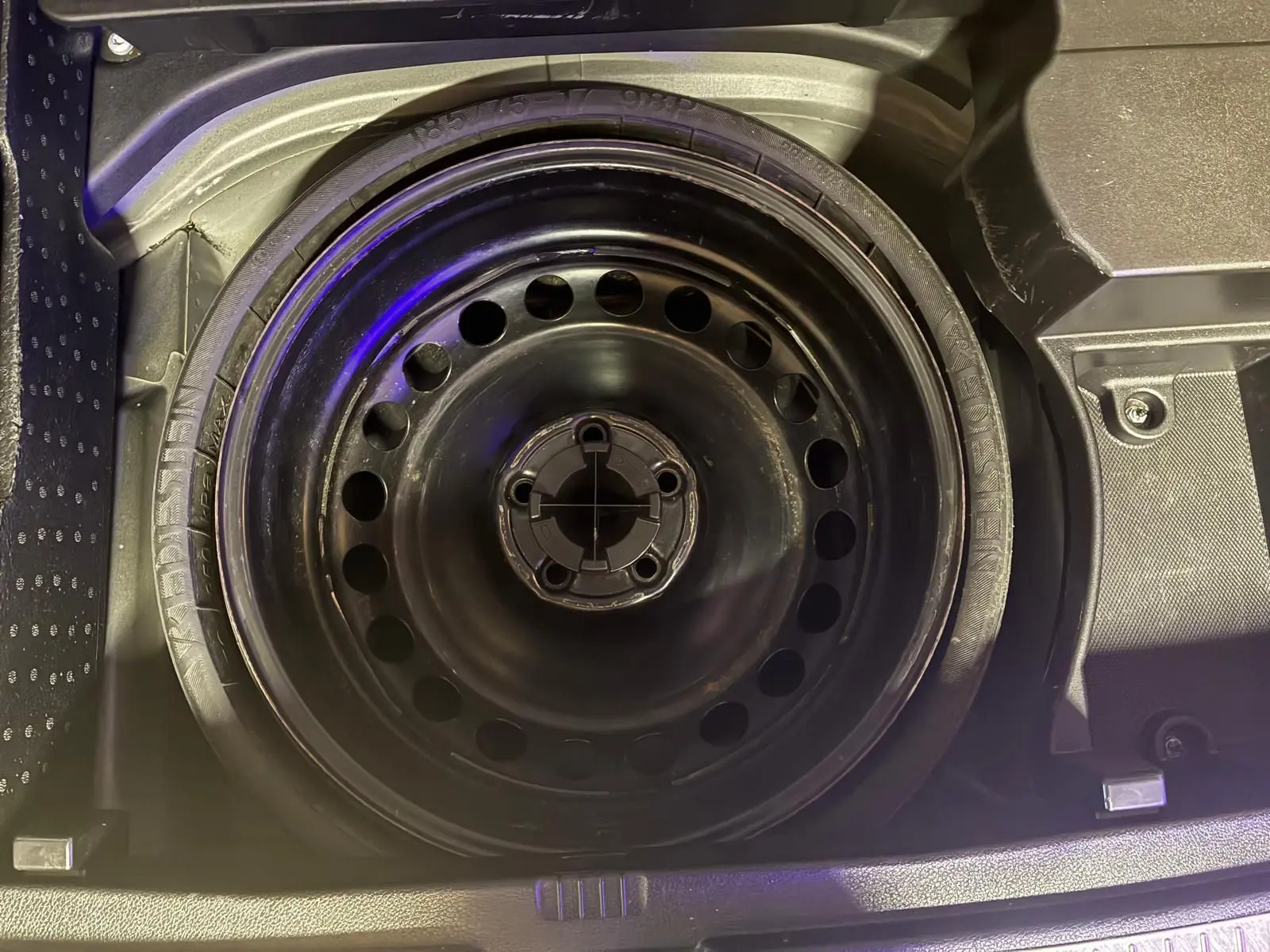 Vue rapprochée de la roue de secours noire en acier dans le coffre d’un Mercedes GLK 220 CDI noir de 2012.