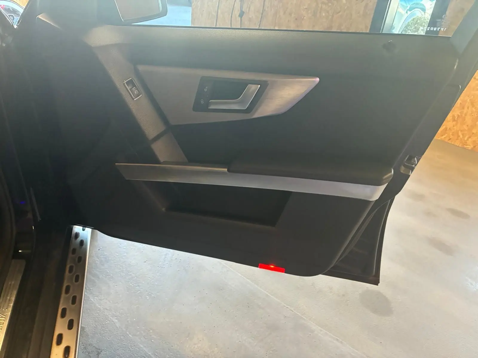 Vue intérieure de la porte côté gauche noire d’un Mercedes GLK 220 CDI avec poignée argentée et éclairage rouge en bas.