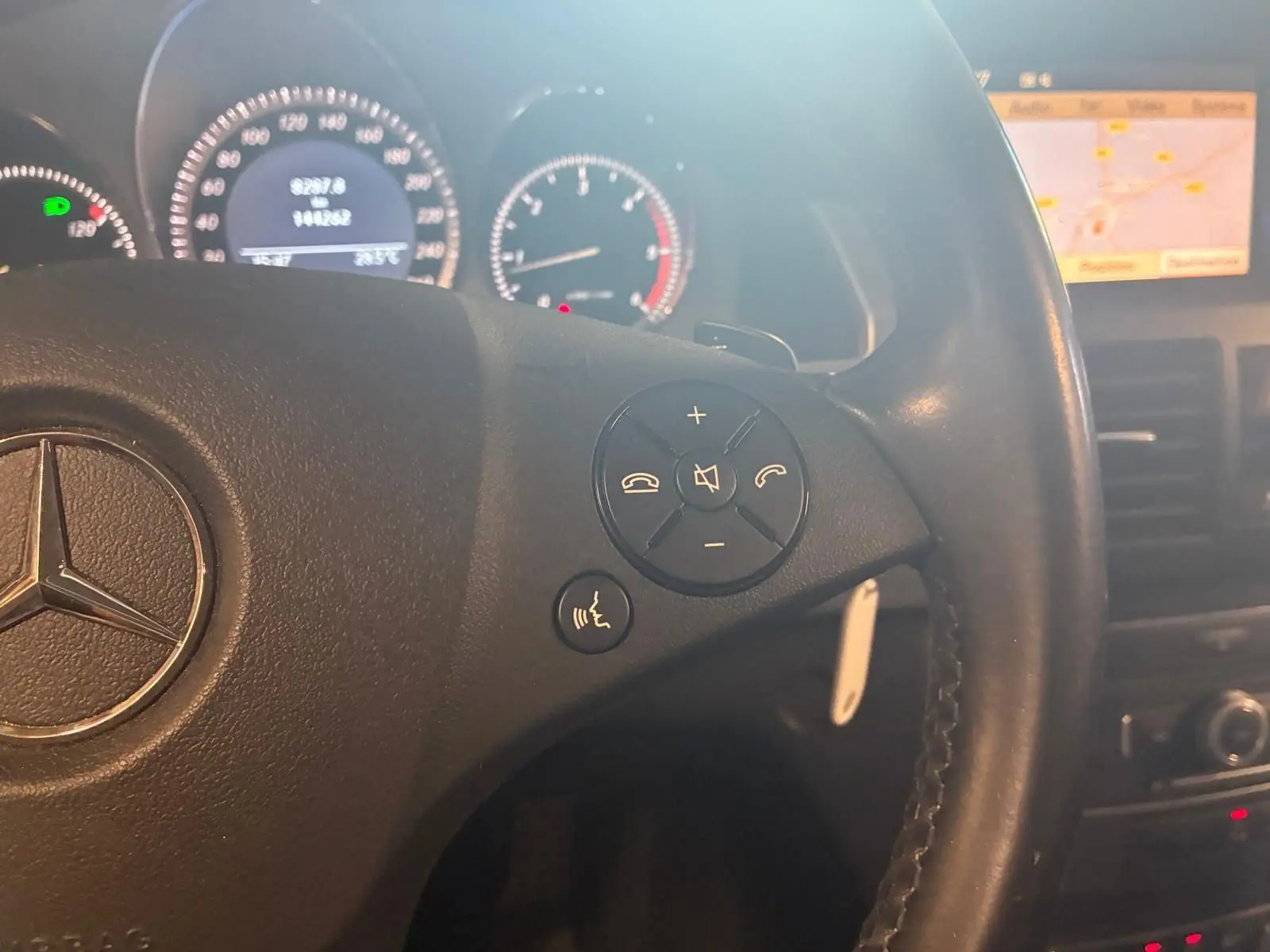Gros plan sur le volant en cuir noir d’un Mercedes GLK 220 CDI 2012, avec commandes audio et écran GPS en arrière-plan.