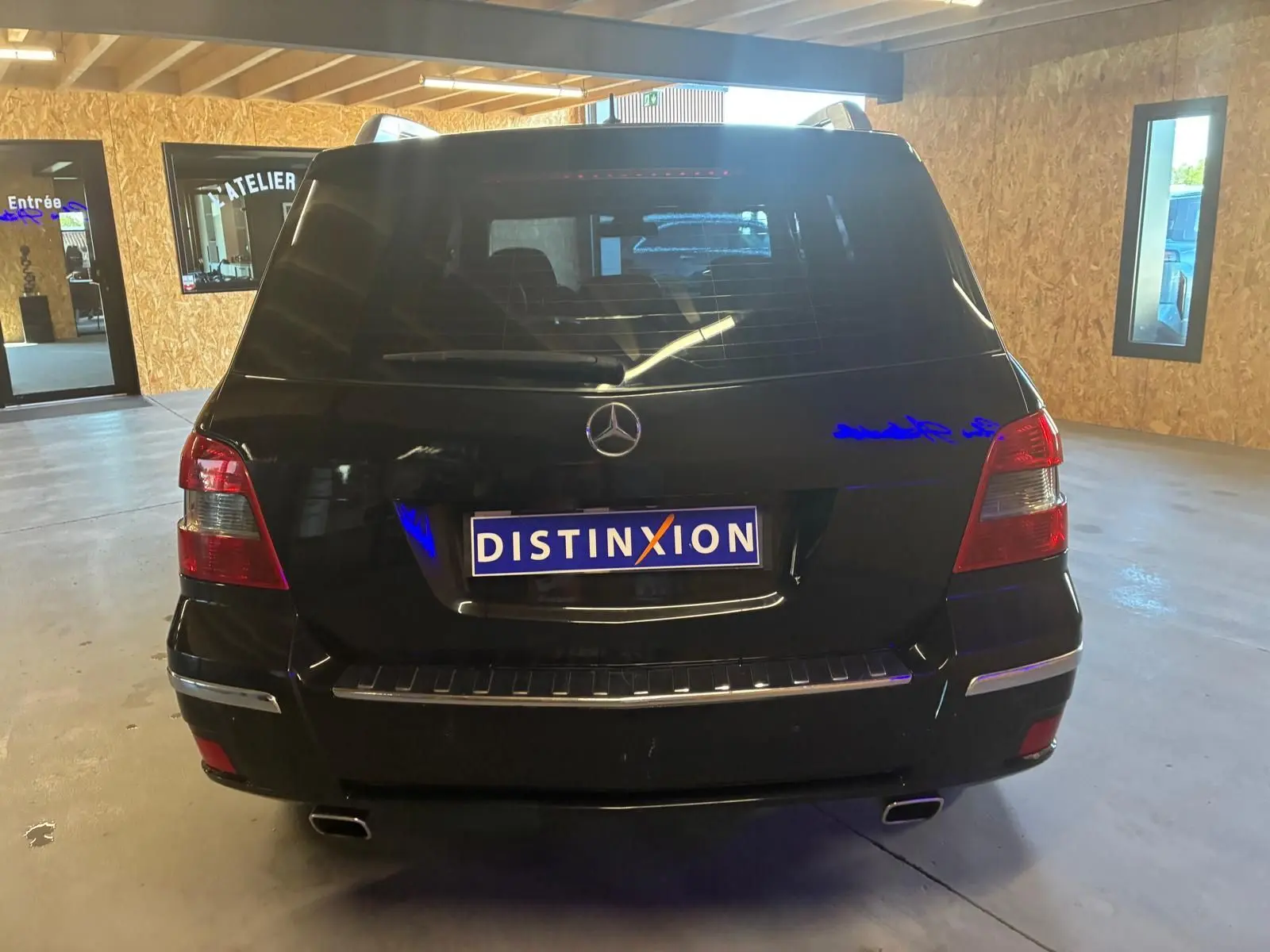 Vue arrière d'un Mercedes GLK noir 2012, avec feux rouges et double sortie d'échappement visible en intérieur d'atelier.